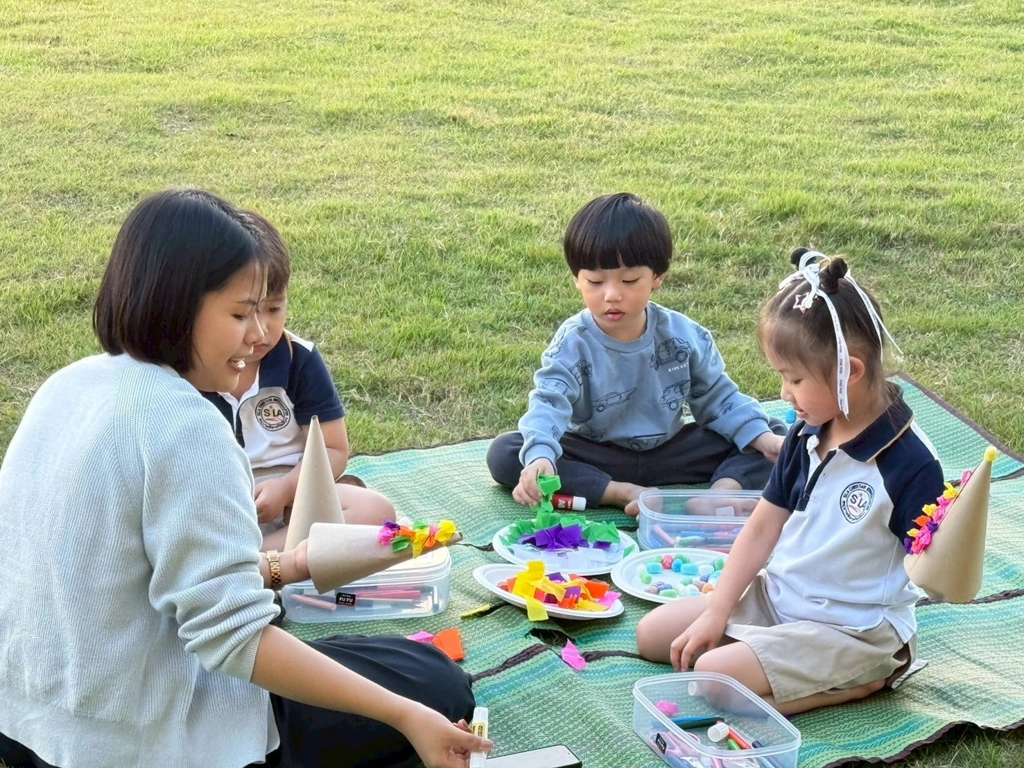 孩子们坐在草地上和老师一起做纸艺