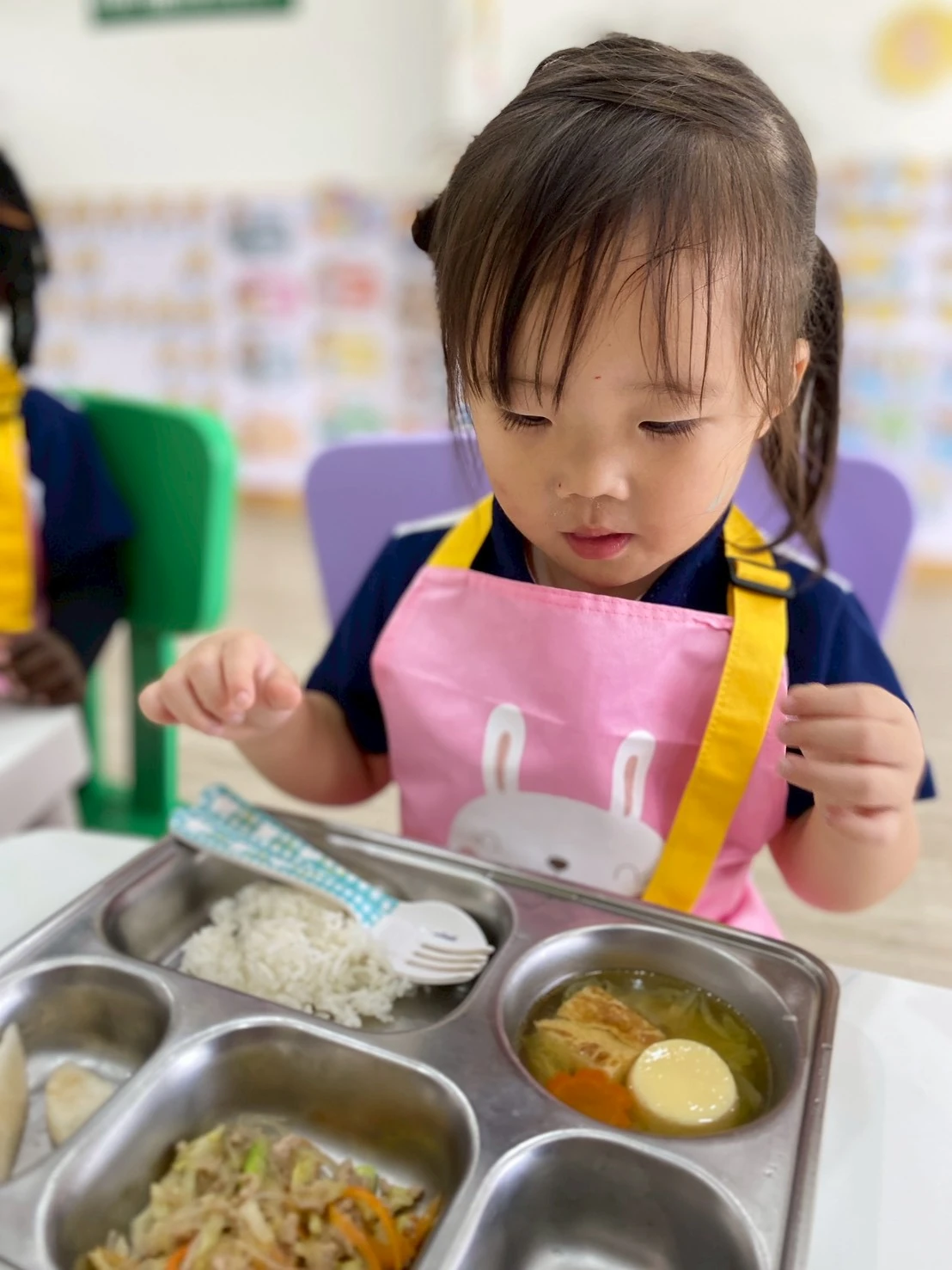 穿着粉色围裙的孩子看着自己的餐盘
