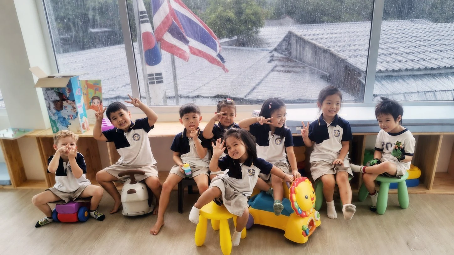 一群 Kindergarten 孩子坐在教室窗边，微笑着向镜头挥手