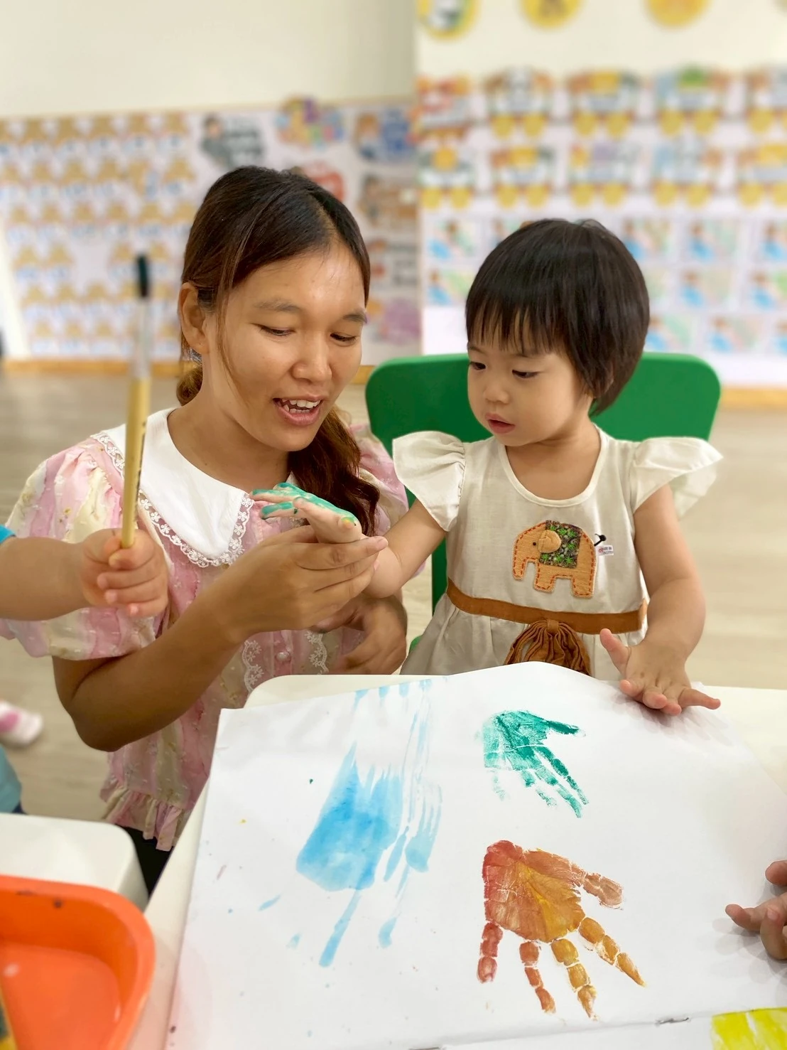 老师温暖微笑，与 Nursery 孩子一起印手印