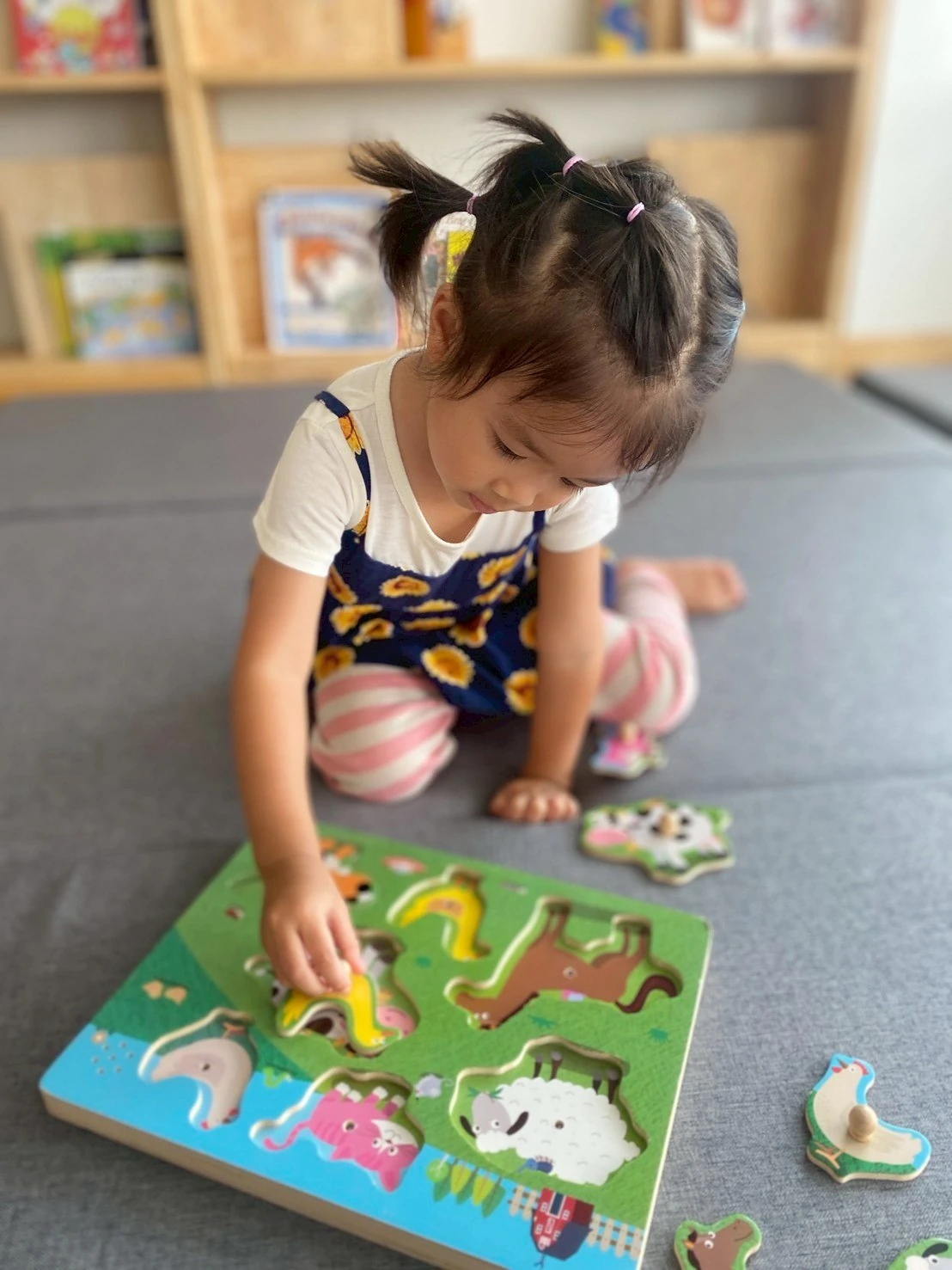 一个 Nursery 女孩跪着专注地玩木质农场动物拼图